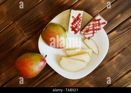 Scheiben rote Birnen und hausgemachte Kuchen sind in einer weißen Platte auf einem Holztisch aus Kiefer Bretter. Frühstücksbuffet im authentischen natürlichen Hotel. Sommer noch lif Stockfoto