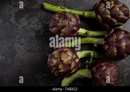 Lila Artischocken blumen Köpfe auf dunklem Schiefer. Stockfoto