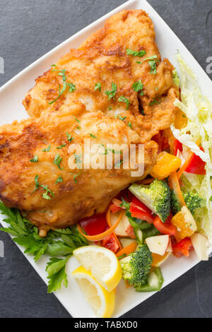 Zwei dicke Filets von Pollack Pollachius pollachius, dass tief in hausgemachter Teig gebraten und serviert mit Obst und rohem Gemüse. Die pollac Stockfoto
