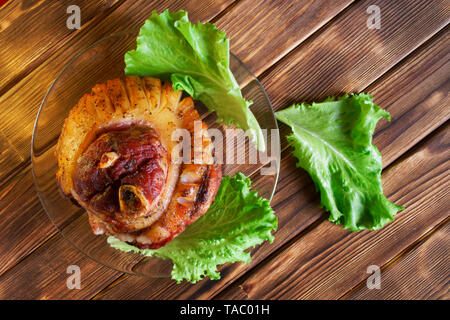 Gebackene mit Gewürzen Fleisch liegt auf einem Holztisch Kiefer Bretter. Eisbein und Salat in eine transparente Platte. Tageslicht. Stockfoto