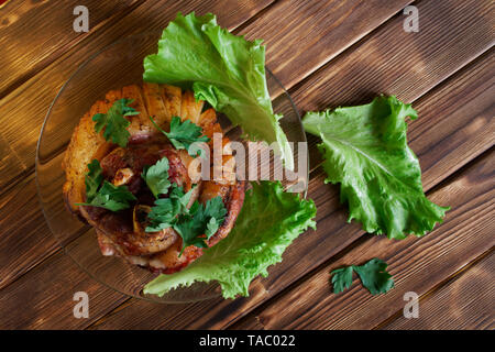 Appetitlich gebackenes Fleisch mit Gewürzen liegt auf einem Holztisch aus Kiefer Bretter. Eisbein, Salat und Petersilie in eine transparente Platte. Tageslicht. Stockfoto