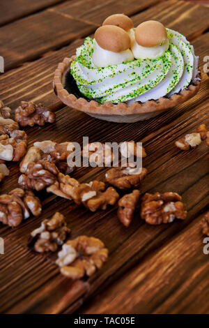 Auf dem hölzernen Tisch ist ein Kuchen in Form eines Korbes mit Protein Creme und Imitation von Pilzen. In der Nähe sind geschälte Walnüsse. Bild vertikal. Stockfoto