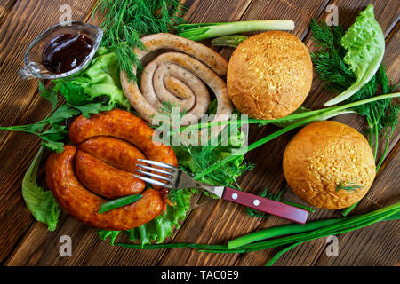 Mais Brötchen, gegrillte Würstchen, und eine transparente Sauce - pan liegen auf einem Holz- Oberfläche mit Gruenen: Salat, Dill, Zwiebel und Petersilie. Picknick - Grill. Vie Stockfoto