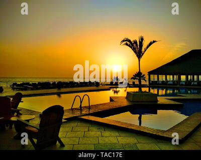 Schöner Pool und Sonnenuntergang Himmel im Senegal, Afrika. Luxuriösen tropischen Strand Landschaft mit Palmen, Liegestühlen und Sonnenliegen.. Es ist tropisches Paradis Stockfoto