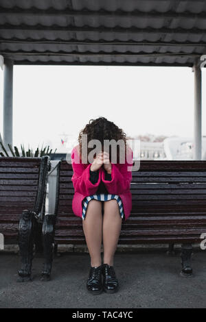 Frau mit lockigem Haar auf einer Bank sitzen Beten Stockfoto