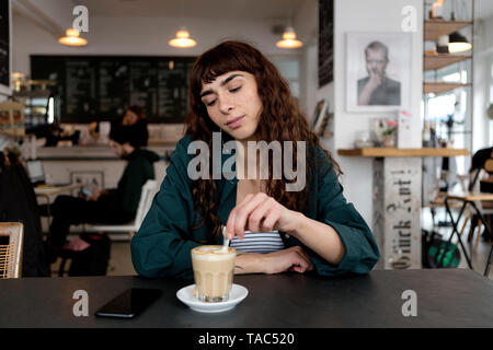 Junge Frau mit Milchkaffee saß am Tisch in einem Cafe Stockfoto