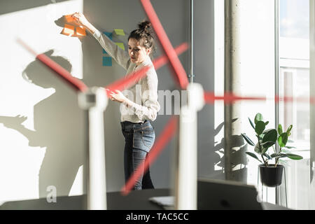 In Office putting Haftnotizen auf Wand mit Wea-Modelle auf dem Schreibtisch Geschäftsfrau Stockfoto