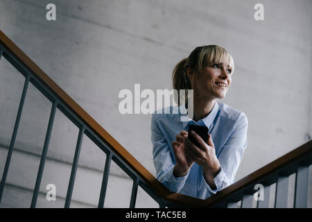 Geschäftsfrau, lehnend auf Geländer, mit Smartphone Stockfoto