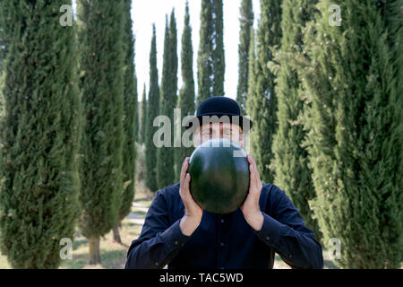Italien, Toskana, Mann von Zypressen tragen eine Melone Holding eine Melone umgeben Stockfoto