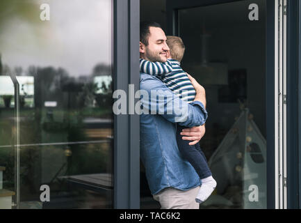 Vater umarmt Sohn an der Terrassentür zu Hause Stockfoto