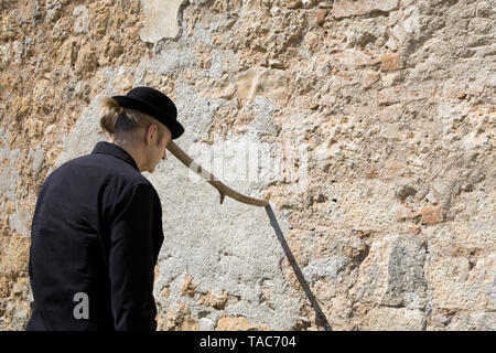 Mann, eine Melone balancing einen Stock an eine Mauer aus Stein Stockfoto