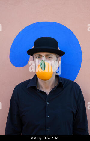 Porträt eines Mannes mit einer Orange an eine Wand mit Fragezeichen tragen eine Melone Stockfoto