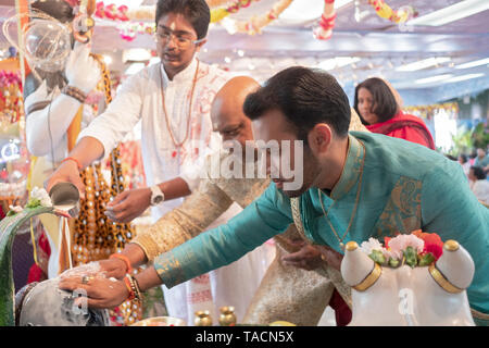 Ein Teenager Pandit und zwei fromme Gläubige gießen Sie Milch über, und tippen Sie auf einen Shiva Lingam an einem Hindu Tempel in Jamaica, Queens, New York. Stockfoto