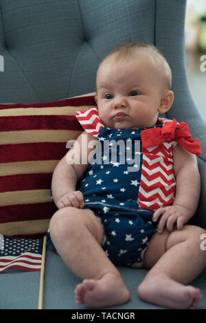 Süße kleine Baby in einem patriotischen USA Outfit in Rot, Weiß und Blau mit dem Sternenbanner der amerikanischen Flagge sitzt auf einem Sofa gekleidet Stockfoto