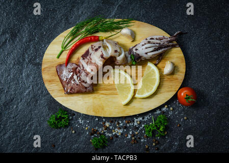 Meeresfrüchte Gegrillter Tintenfisch mit Kräutern und Gewürzen Zitronen Tomaten chili Knoblauch und Dill auf Schneidebrett dunklen Hintergrund/Squid das Restaurant Meer serviert Stockfoto