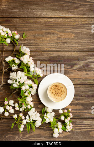 Eine heiße Tasse aromatischen Kaffee und einem blühenden Zweig von einem Apfelbaum auf einer hölzernen Hintergrund. Flache Layout. Stockfoto