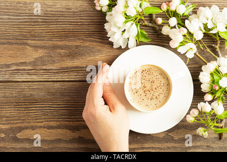 Eine heiße Tasse aromatischen Kaffee in weibliche Hände und ein blühender Apfelbaum Filiale auf einer hölzernen Hintergrund. Flache Layout. Stockfoto