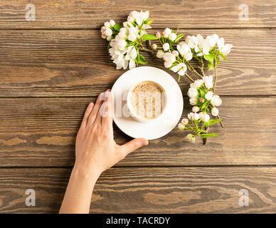 Eine heiße Tasse aromatischen Kaffee in weibliche Hände und ein blühender Apfelbaum Filiale auf einer hölzernen Hintergrund. Flache Layout. Stockfoto