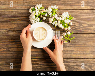Eine heiße Tasse aromatischen Kaffee in weibliche Hände und ein blühender Apfelbaum Filiale auf einer hölzernen Hintergrund. Flache Layout. Stockfoto