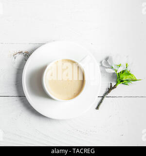 Eine heiße Tasse aromatischen Kaffee und blühende Zweige von einem Apfelbaum auf einer hölzernen weißen Hintergrund. Flach. Stockfoto