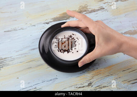 Schwarze Tasse Kaffee mit Milch. Woman's Hände, die Tasse mit Kaffee, Ansicht von oben. Stockfoto