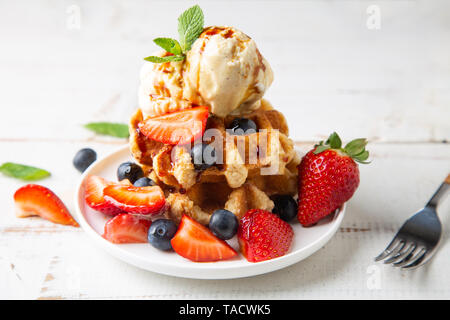 Stapel von Waffeln mit Erdbeeren, Brombeeren und Vanille Eis und Karamell Sirup auf einem weißen Tisch Stockfoto