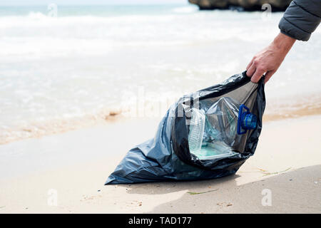 Nahaufnahme von einem kaukasischen Mann Müll sammeln auf einem einsamen Strand, neben dem Wasser, als Aktion, um die natürliche Umgebung zu reinigen Stockfoto