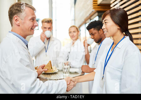 Leitender Arzt begrüsst Medizin Studenten oder jungen asiatischen Kollegen mit Handshake Stockfoto