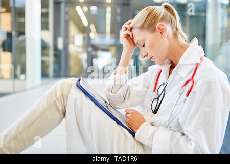Junge Ärztin oder Krankenschwester sitzt durch die Überlastung im Krankenhaus müde Stockfoto