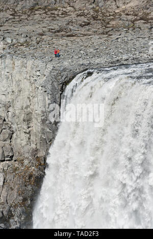 Dettifoss im Nordosten Islands, den mächtigsten Wasserfall Europas. Zwei Touristen stehen auf der Ostseite oberhalb der steilen Klippen neben dem 44 m drop Stockfoto