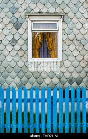 Akureyri, North Island. Detail eines alten Hauses mit abgerundeten Schiefer Schindeln in einen Fisch Skala Muster bedeckt, mit einem blauen Garten Zaun vor Stockfoto