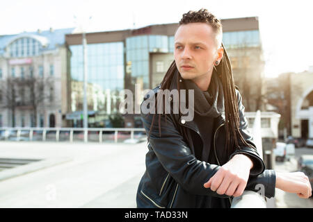 Rocker Rock Star jungen kaukasischen Mann mit Dreadlocks gehen auf die Straße der Stadt Herbst Tag. In das Leder Jacke angezogen Stockfoto