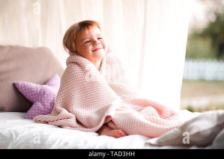 Lächelnden Mädchen 2-3 Jahre alten im Bett sitzen draußen in der Decke eingewickelt. Stockfoto