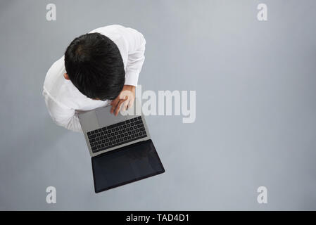 Legerer Mann wotk auf Laptop mit dunklen Haaren auf grauem Hintergrund über der oberen Ansicht isoliert Stockfoto