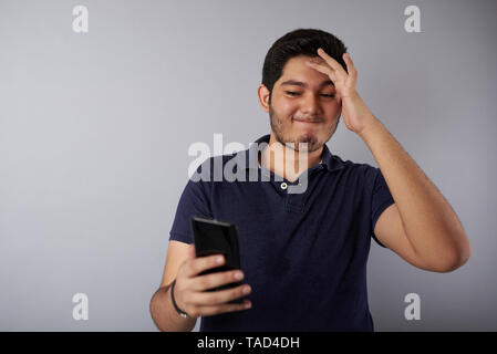 Schlechte Nachrichten auf dem Smartphone lesen junger Mann auf Grau studio Hintergrund Stockfoto