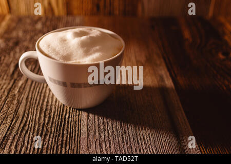 Frisch Kaffee mit Sojamilch Schaum in eine weiße Tasse mit rustikalen bräunlich Holz- Hintergrund in der schönen Moody Morgensonne gebraut Stockfoto