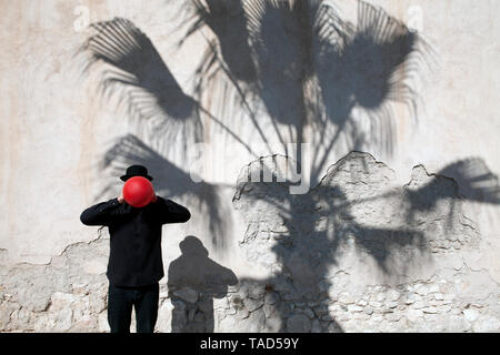 Marokko, Essaouira, Mann, eine Melone mit roten Ballon vor seinem Gesicht an der Wand Stockfoto