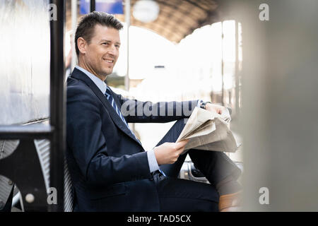 Lächelnd Geschäftsmann lesen Zeitung auf Bahnsteig Stockfoto