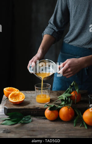Junger Mann gießen frisch gepressten Orangensaft in ein Glas, Teilansicht Stockfoto