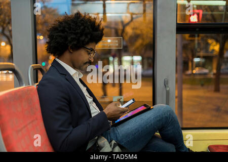 Spanien, Barcelona, Geschäftsmann, der in die Straßenbahn bei Nacht mit Handy und Tablet Stockfoto