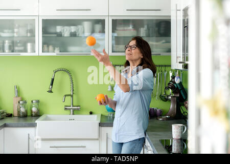 Reife Frau jonglieren mit Orangen in der Küche zu Hause. Stockfoto