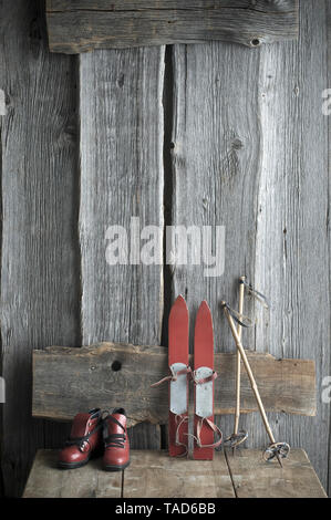 Der alte Kinder Skier, Stöcke und Skischuhe stehend auf holzbank Stockfoto