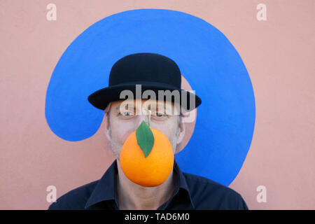Porträt eines Mannes mit einer Orange an eine Wand mit Fragezeichen tragen eine Melone Stockfoto