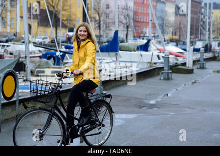 Dänemark, Kopenhagen, glückliche Frau Reiten Fahrrad am Hafen der Stadt im regnerischen Wetter Stockfoto