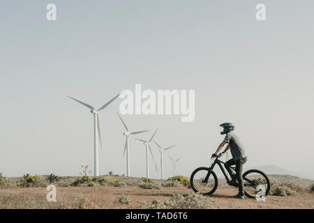 Spanien, Lanzarote, Mountainbiker auf einer Reise in Wüstenhaft Landschaft mit Windkraftanlagen im Hintergrund Stockfoto