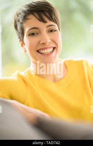 Portrait von Frau mit kurzen braunen Haaren tragen gelbe Pullover auf der Couch zu Hause sitzen Stockfoto