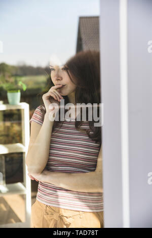 Porträt der nachdenkliche junge Frau hinter Fensterscheibe Stockfoto
