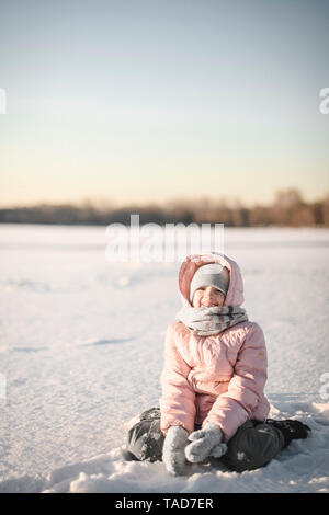 Portrait von kleines Mädchen sitzt im Schnee Stockfoto