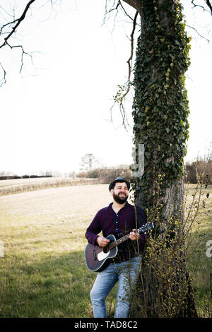 Mann Gitarre zu spielen, ein Baum auf der Wiese Stockfoto