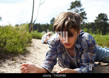 Junge liegend auf sandigen Weg beobachten Käfer Stockfoto